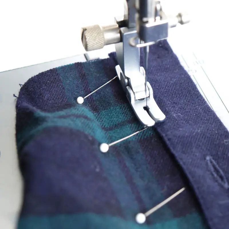Tailor pinning navy plaid wool fabric under a sewing machine presser foot for alteration