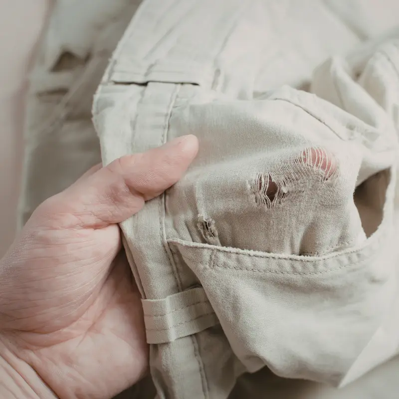 Hand showing a torn pair of pants in need of alteration repair